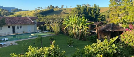 Una propiedad residencial con piscina, un pequeño jardín y una colina al fondo.