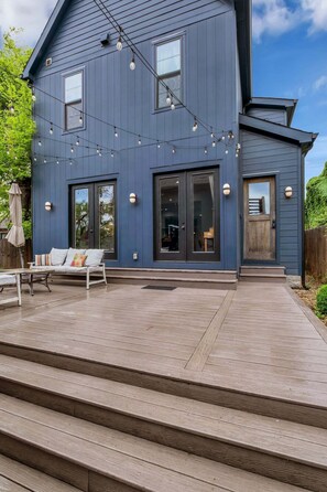 A two-story house with a covered patio area, a sofa, and a dining table.