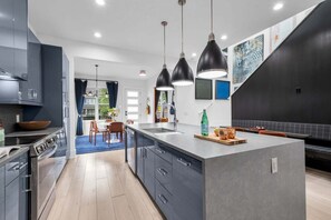 A modern kitchen with a central island, pendant lighting, and a view to a dining area.