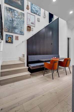 A modern interior with a staircase leading to a dark-toned seating area, a dining table with orange chairs, and various artworks on the walls. - Southern Souls 715-Downtown Nearby-Sleeps 6 (Nashville)