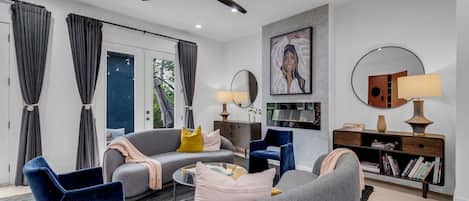 Uma sala de estar moderna com um sofá cinza, poltronas azuis, uma mesa de centro e uma estante de livros.