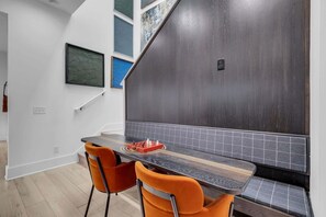 Une cuisine moderne avec un mur d’accent en bois foncé, un plan de travail noir et des chaises orange.