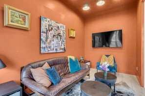 Un salón con un sofá de cuero, una mesa de centro y un sillón azul. Hay dos cuadros en la pared y un televisor.
