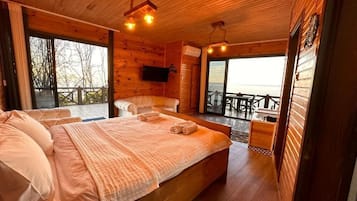 Uma cabana de madeira com uma cama grande, uma televisão presa na parede e uma varanda com vista.