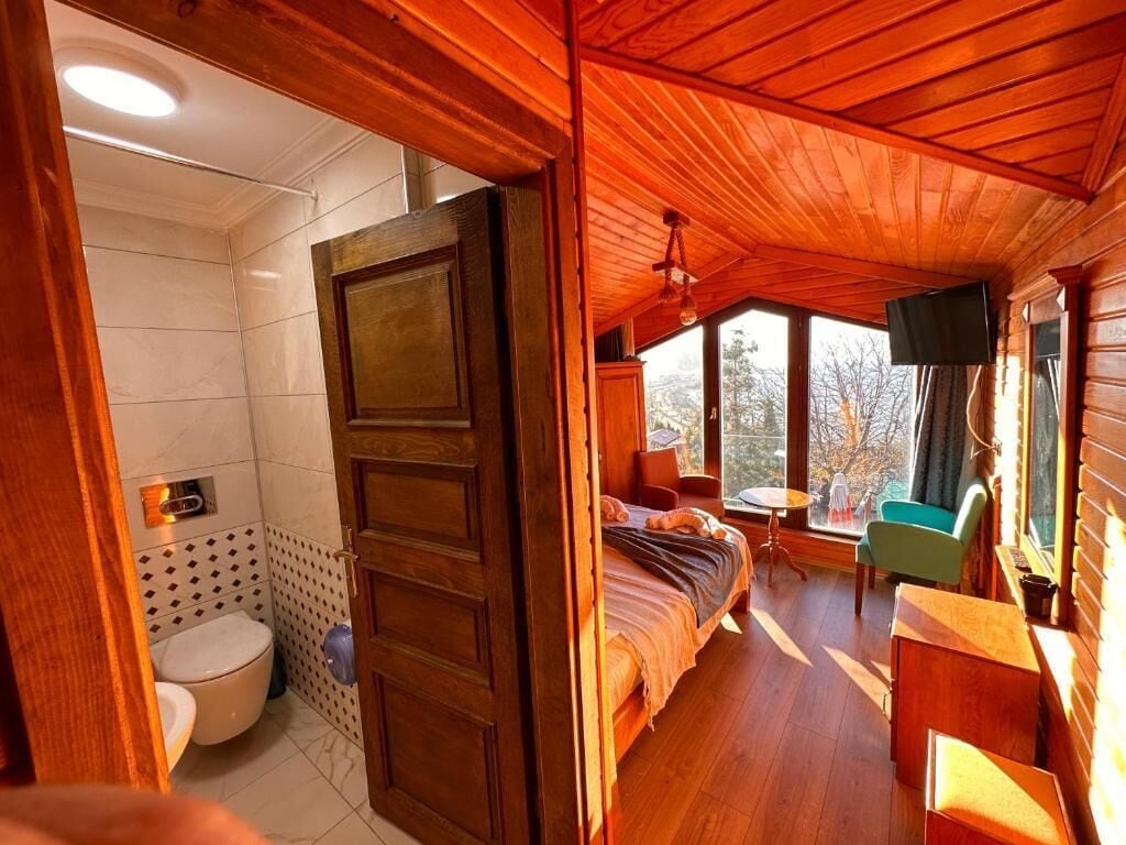 Interior de una cabaña de madera con baño, cama, televisor y una mesita.