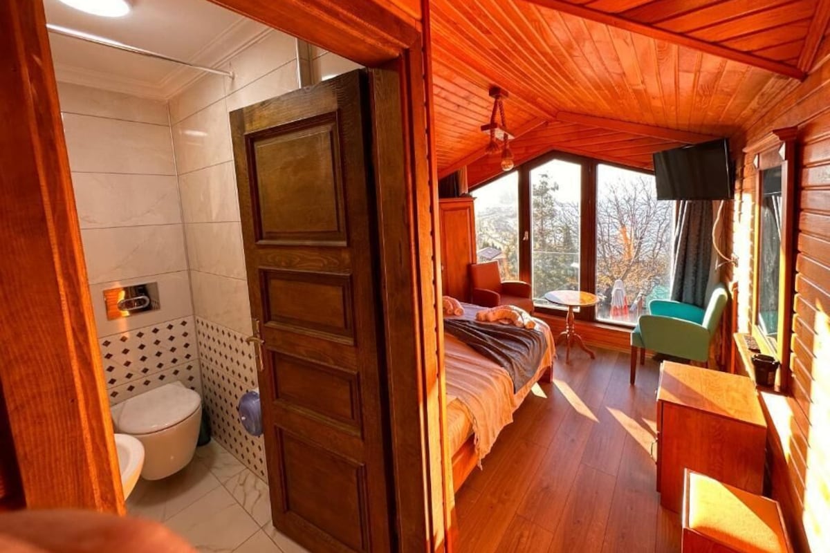 Interior de una cabaña de madera con baño, cama, televisor y una mesita.