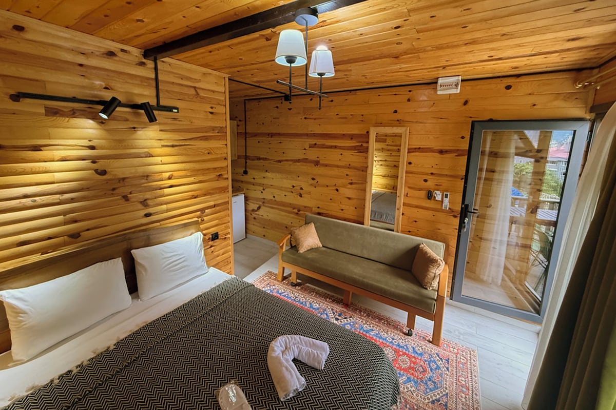 Habitación de cabaña de madera con cama, sofá, espejo y puerta que da al exterior.