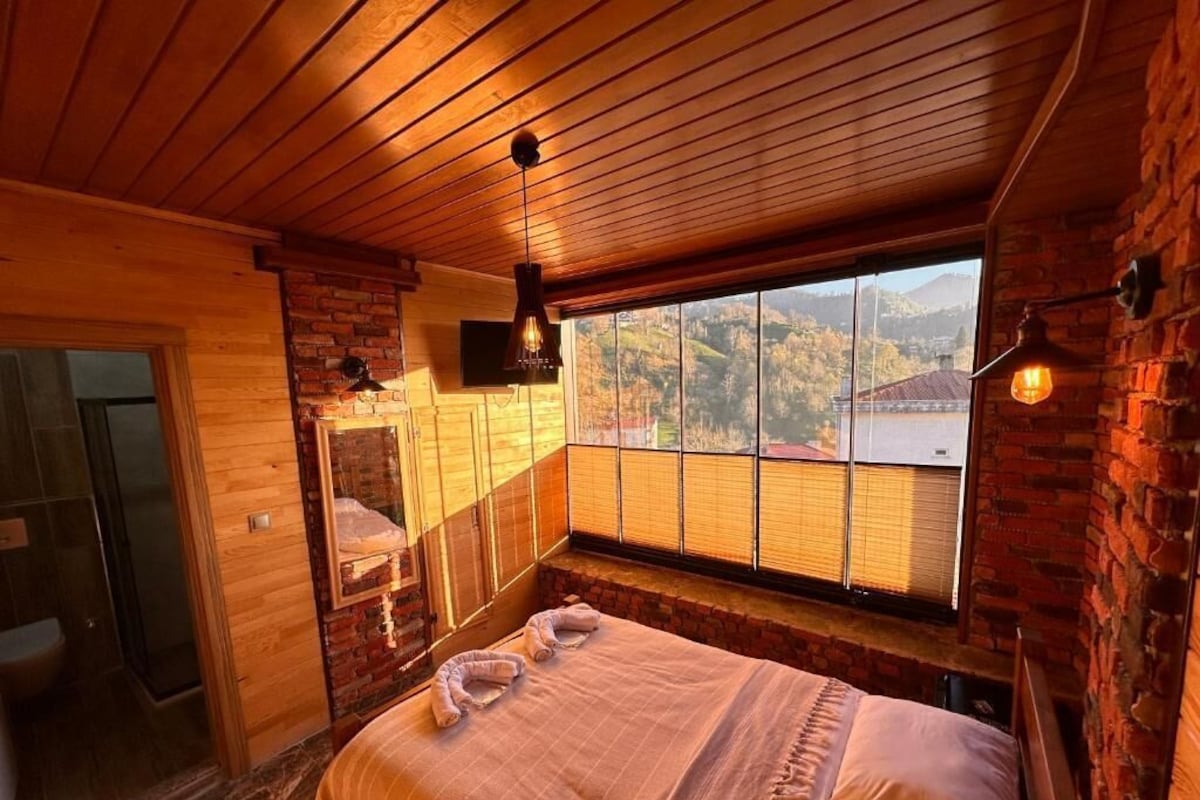 Un dormitorio con un ventanal grande, techo de madera y pared de ladrillo.