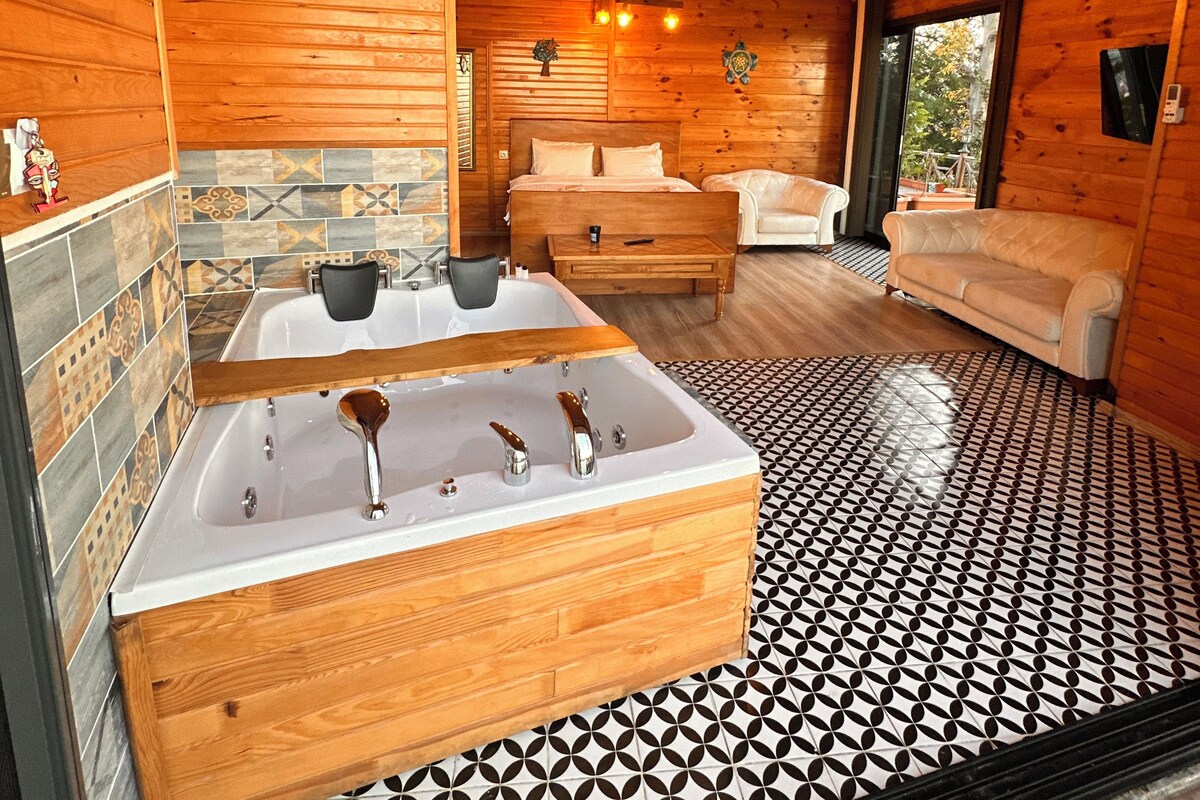 A wooden cabin interior with a large bathtub, a sofa, and a dining table.