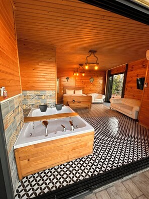 A wooden cabin interior with a large bathtub, a sofa, and a dining table.