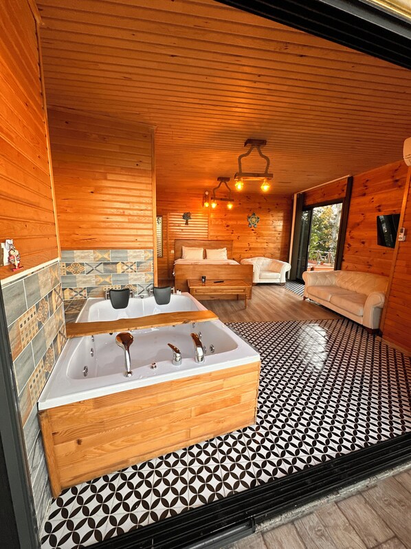 A wooden cabin interior with a large bathtub, a sofa, and a dining table.