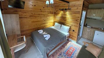 Une pièce aux murs lambrissés, comprenant un lit, un petit bureau, une chaise et un coin cuisine.