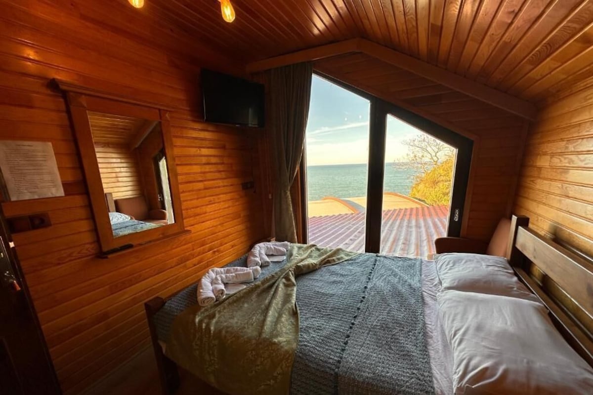 Un dormitorio de cabaña de madera con una cama, un televisor y vista al mar.