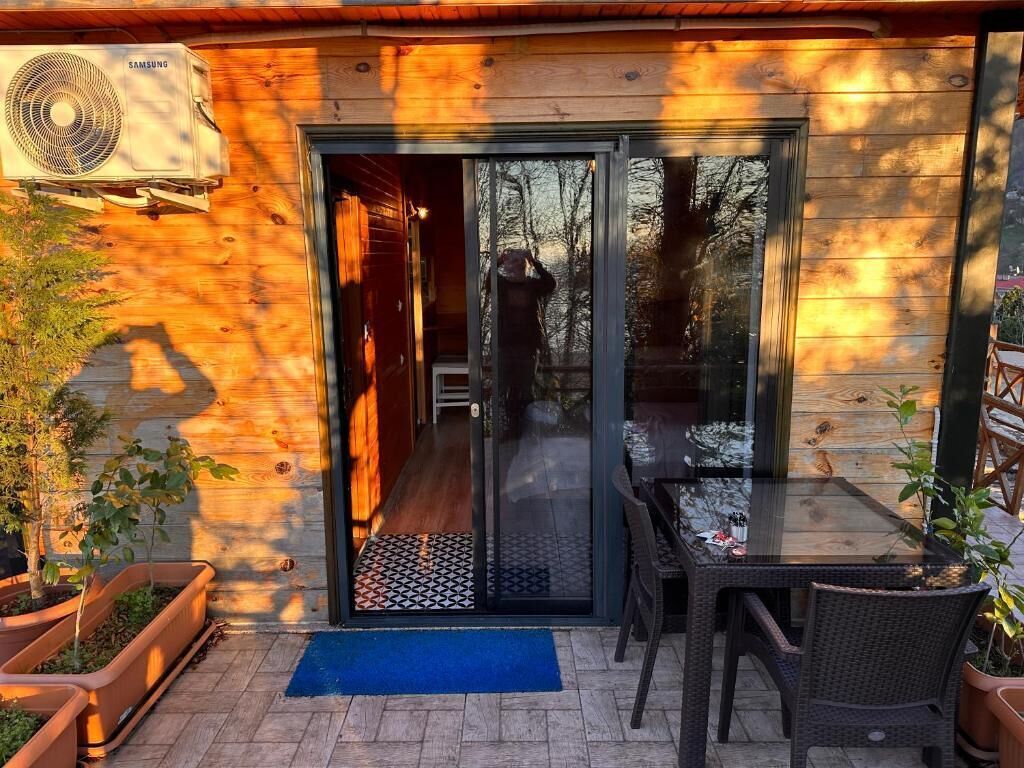 Una cabaña de madera con un ventanal de vidrio que da a un patio con mesa y sillas.