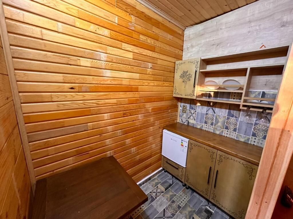 Una cocina compacta con paredes de madera, salpicadero de azulejos y un refrigerador pequeño.