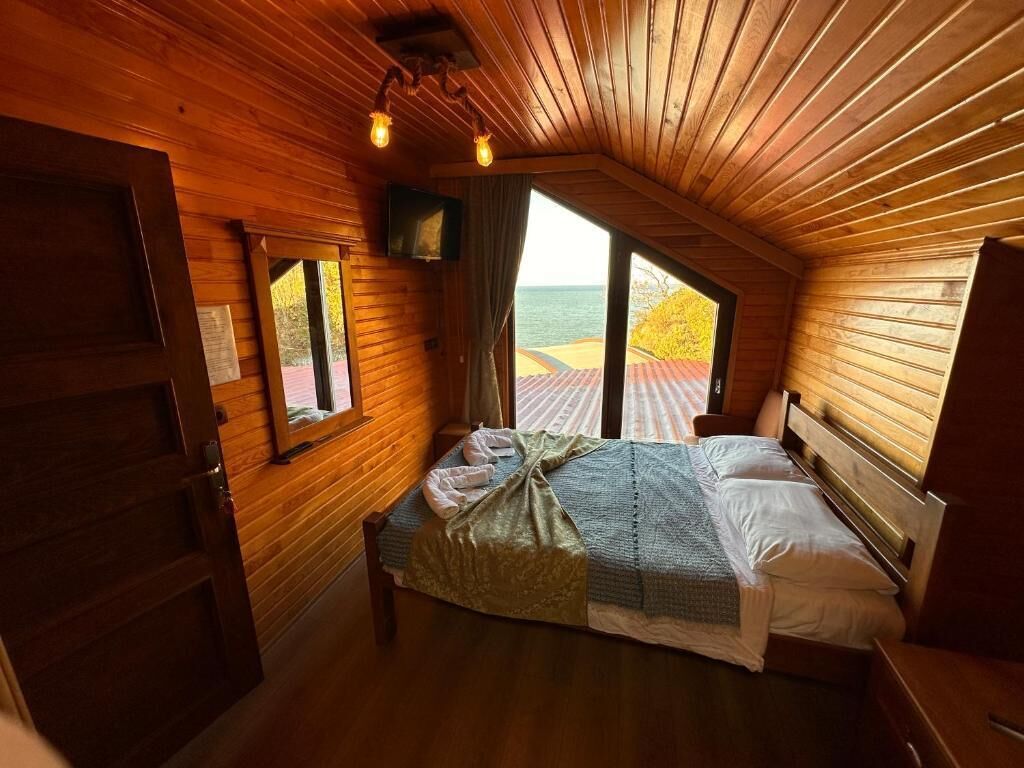 Une chambre dans une cabane en bois, avec un lit, une télévision et vue sur la mer.