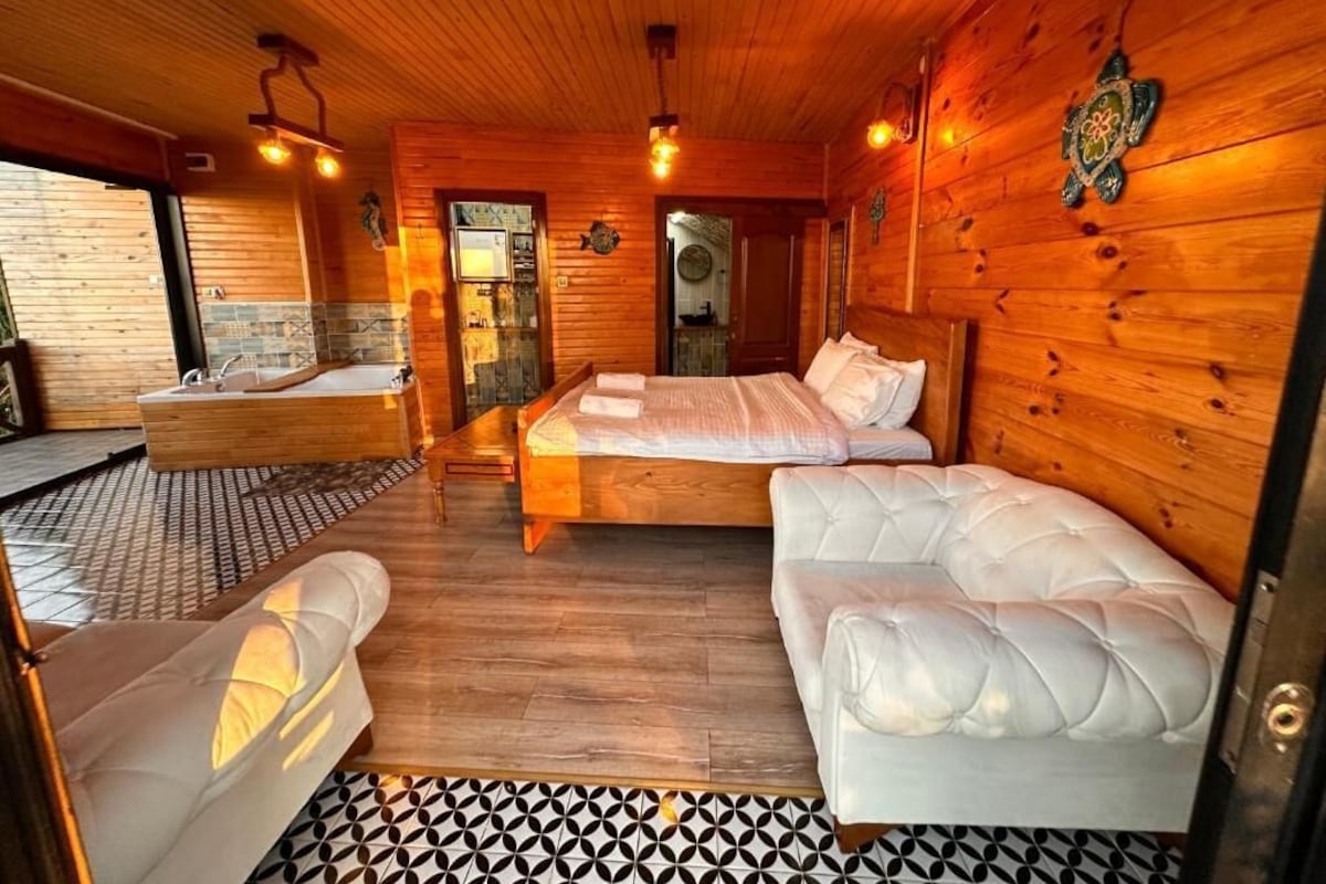 Interior de una cabaña de madera con una cama, un sofá, una bañera y un piso con diseño.