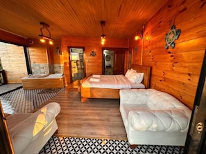 Interior de una cabaña de madera con una cama, un sofá, una bañera y un piso con diseño.