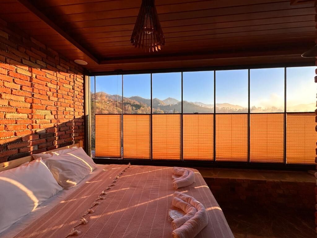 A room with a bed, a brick wall, and a large window with a view of mountains.
