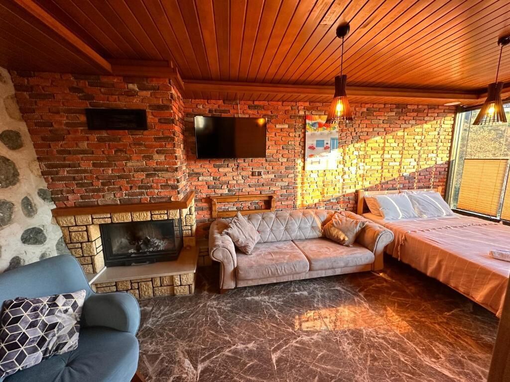 A cozy room with a brick fireplace, a sofa, a bed, and a television mounted on the wall.