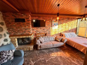 A cozy room with a brick fireplace, a sofa, a bed, and a television mounted on the wall. - Falez Cafe Restorant Pansiyon - Arhavi (Arhavi)