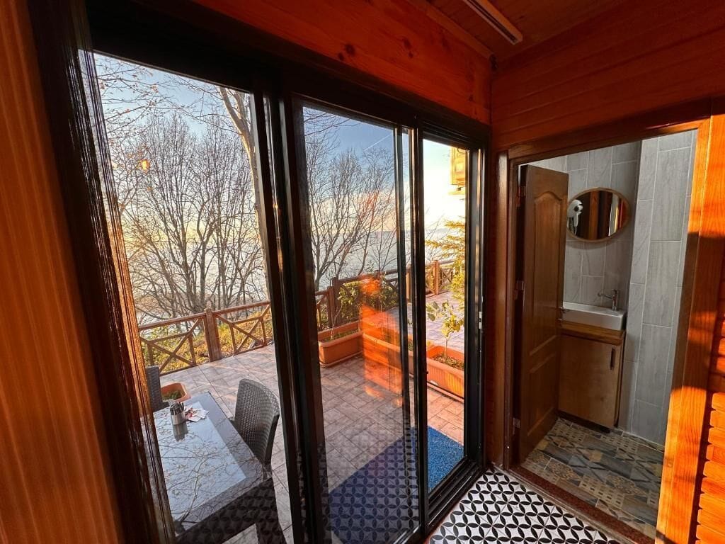 Ein Zimmer mit einer Schiebetür zu einer Terrasse im Freien, die einen Tisch und Stühle, eine Holzbalkendecke und einen gefliesten Boden bietet.
