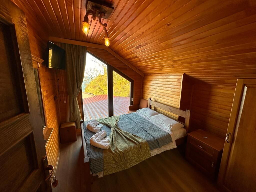 Ein gemütliches Zimmer mit Holzboden, einem Bett mit grüner Decke, einem Holzschrank und einem Fernseher an der Wand.