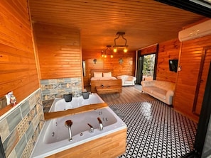 Interior de una cabaña de madera con una bañera grande, un sofá y una mesa de comedor.