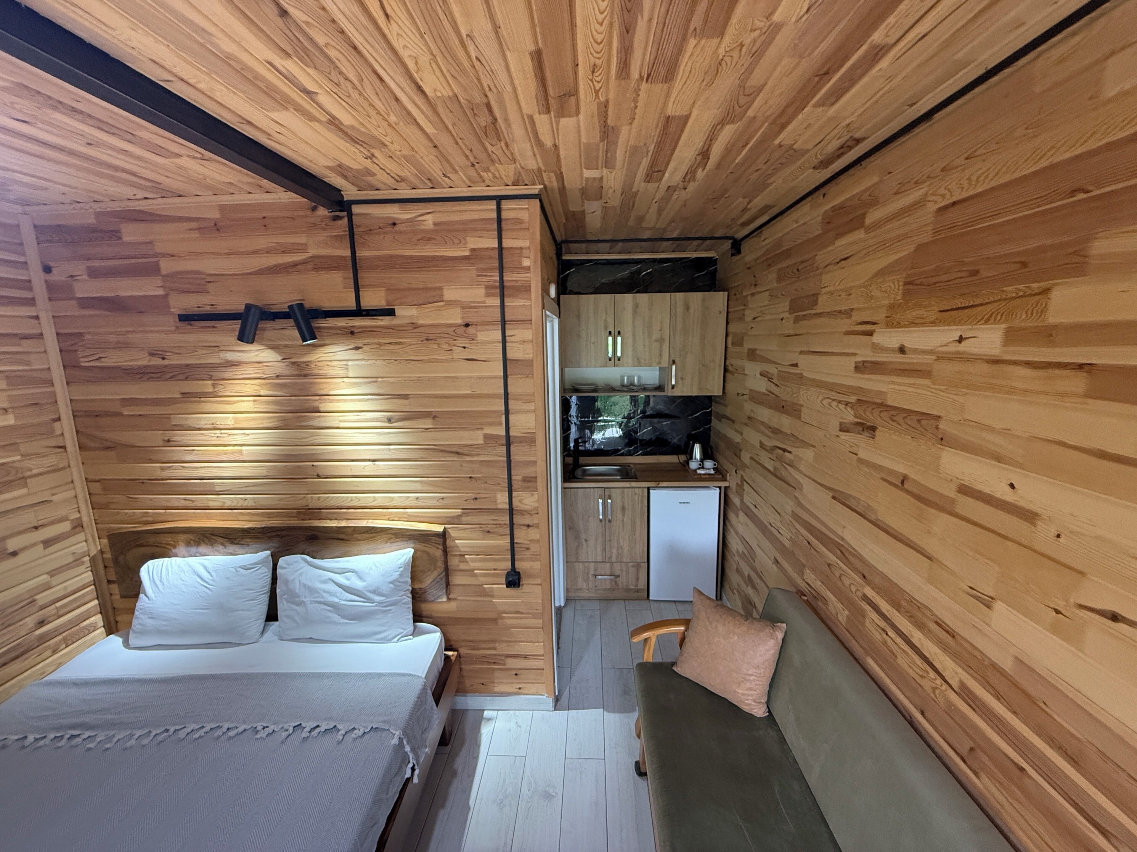 Una habitación pequeña con cama, sofá, kitchenette y paredes de madera.