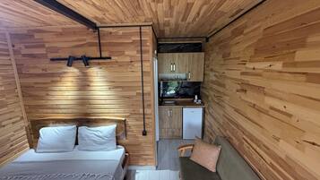 Una habitación pequeña con cama, sofá, kitchenette y paredes de madera.
