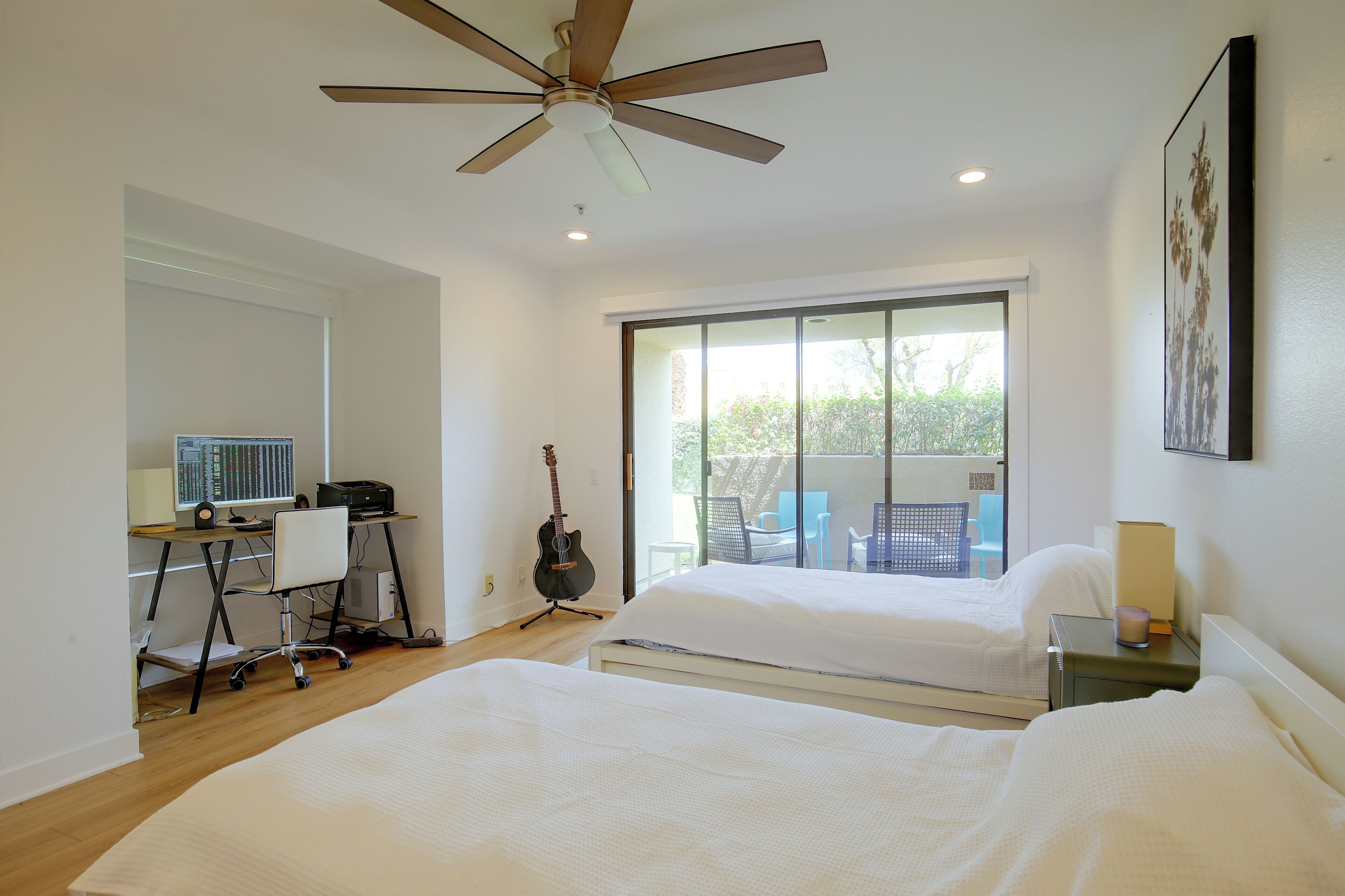 Une chambre avec deux lits, un bureau avec un ordinateur, une guitare et un balcon avec des chaises.