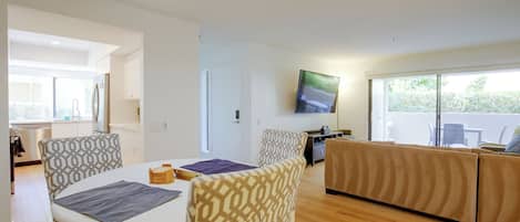 Una sala de estar moderna con comedor, un conjunto de sofás y un televisor de pantalla plana montado en la pared.