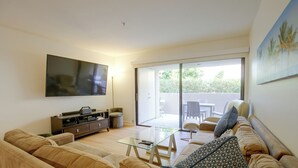 A modern living room with a flat-screen TV, a glass coffee table, a sofa, and a sliding glass door leading to an outdoor area. - Unwind Poolside, Walk Dtwn! Palm Springs Retreat (Palm Springs)