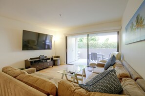 A modern living room with a flat-screen TV, a glass coffee table, a sofa, and a sliding glass door leading to an outdoor area. - Unwind Poolside, Walk Dtwn! Palm Springs Retreat (Palm Springs)