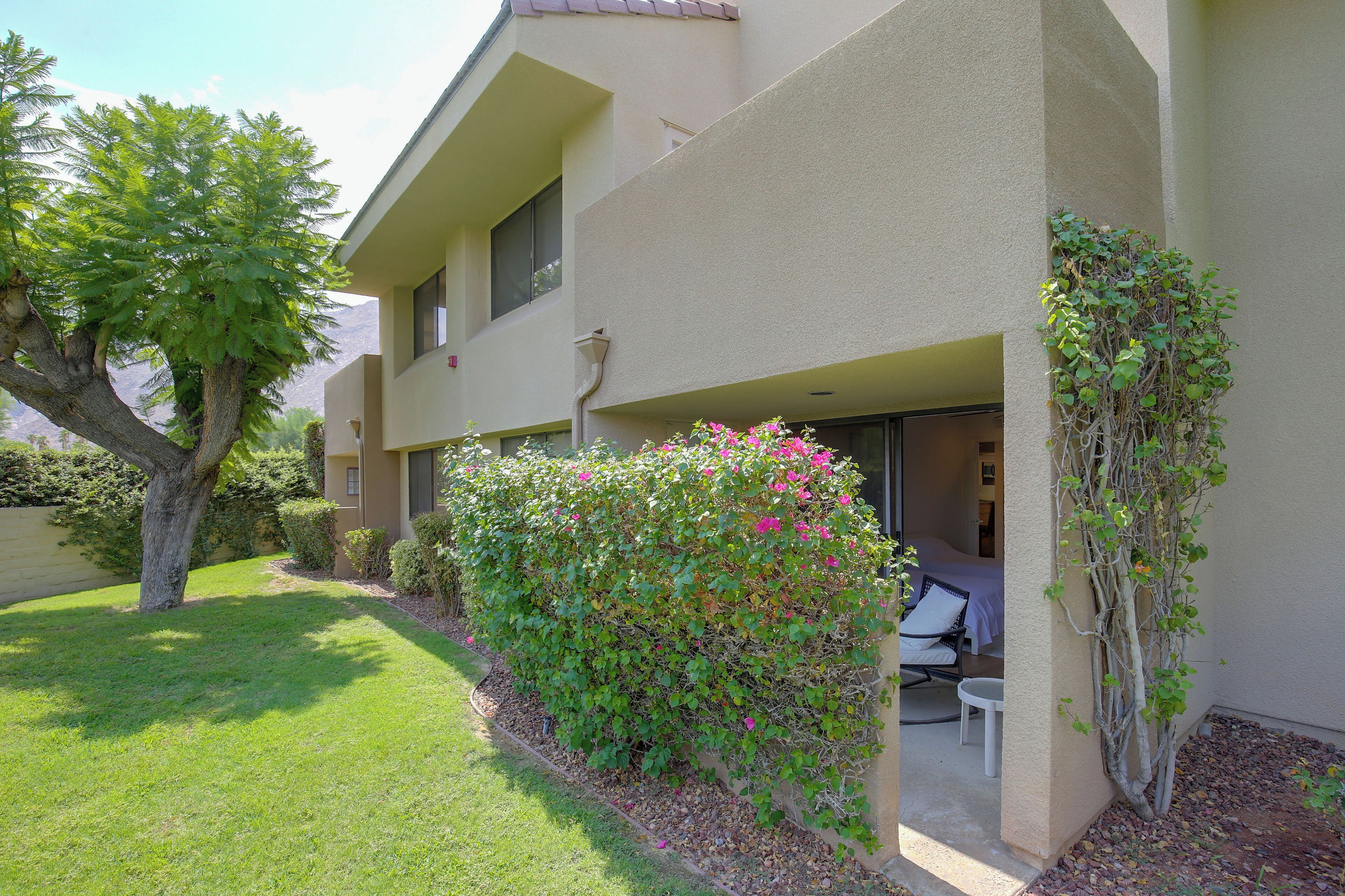 A two-story building with a covered outdoor seating area, a small garden, and a view of the mountains.