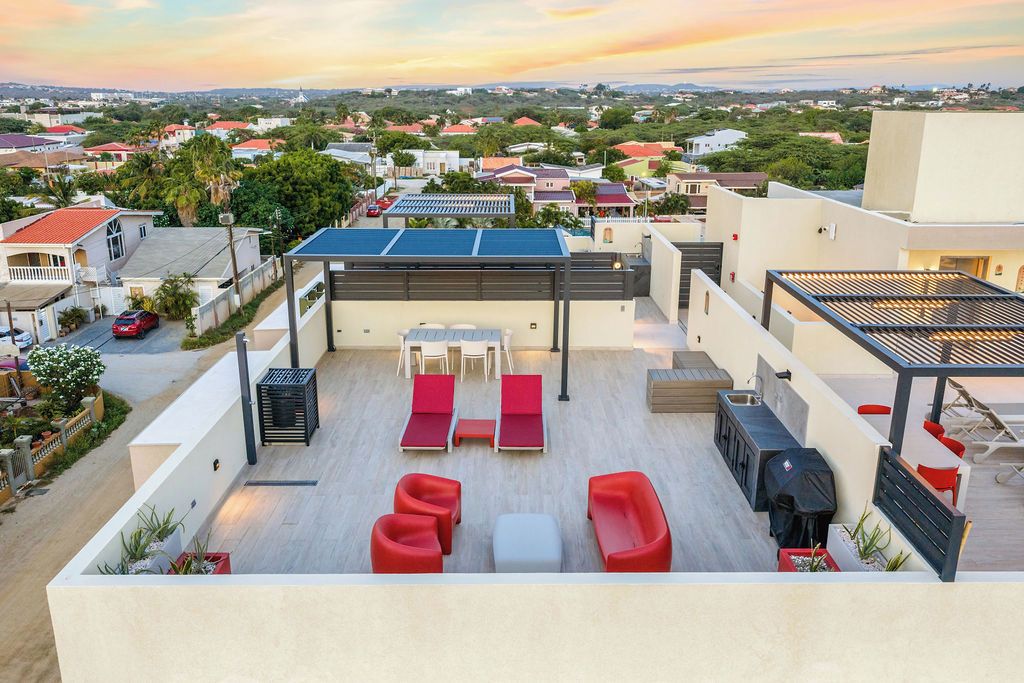 Eine Dachterrasse mit Gartenmöbeln, einem Grill und Blick auf eine Wohngegend.