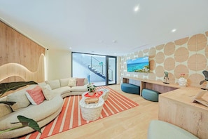 A modern living room with a curved sofa, a coffee table, and a TV on the wall. - Bonsai Studio-Airy 202 (Noord)