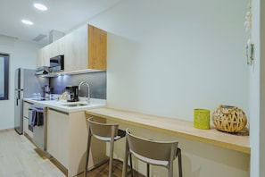 A modern kitchen with a built-in microwave, coffee maker, and a small island with bar stools. - Bonsai1BR Suite-Coastal 104 (Noord)