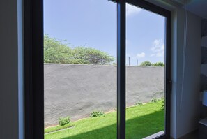 A view through a window with a concrete wall and a grassy area outside. - Bonsai1BR Suite-Coastal 104 (Noord)
