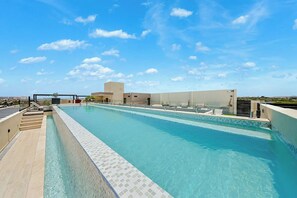 A rooftop swimming pool with clear blue water, surrounded by a tiled deck and a clear sky. - Bonsai 1BR Suite-Blue Glow 105 (Noord)