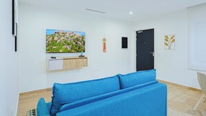 Un soggiorno moderno con un divano blu, una televisione a schermo piatto montata a parete, un piccolo mobile e una porta nera.