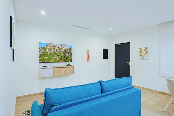 Uma sala de estar moderna com um sofá azul, uma TV de tela plana na parede, um pequeno armário e uma porta preta.