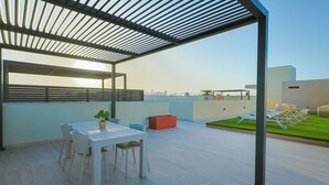 Una terrazza sul tetto con tavolo e sedie, una pianta in vaso e un fioriere rosso.