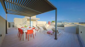 Une terrasse sur le toit dotée d’un espace repas couvert, de chaises longues et offrant une vue dégagée sur le panorama urbain.