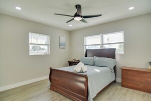 Un dormitorio con cama, mesita de noche, cómoda, ventilador de techo y dos ventanas con persianas.