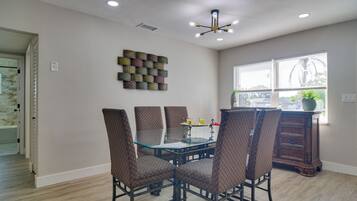 A dining area with a glass table and patterned chairs, a decorative wall piece, and a window with blinds.