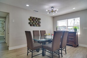 Un comedor con una mesa de vidrio y sillas estampadas, un adorno en la pared y una ventana con persianas.