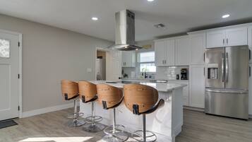 Una cocina moderna con alacenas blancas, un refrigerador de acero inoxidable y cuatro taburetes de madera.