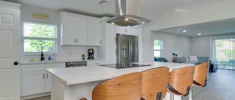 Una cocina moderna con armarios blancos, un refrigerador de acero inoxidable y una isla central con taburetes de bar.
