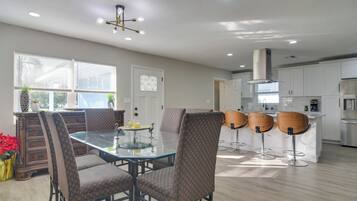 A modern kitchen with white cabinets, a glass-top dining table, and four bar stools.
